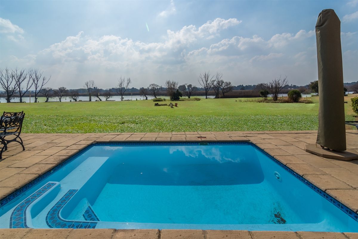 A well-maintained swimming pool with paved surround, overlooking a spacious lawn and scenic waterfront views.