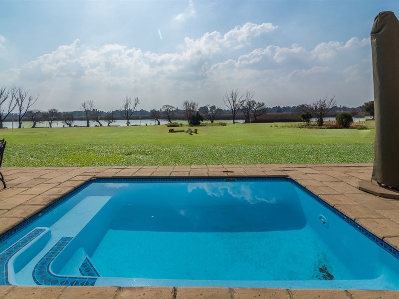 A well-maintained swimming pool with paved surround, overlooking a spacious lawn and scenic waterfront views.