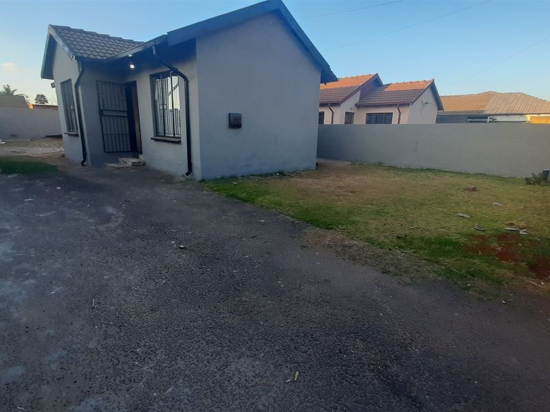 Rear view of the property featuring a paved driveway, a small lawn area, and a secure entrance with security bars and gate.