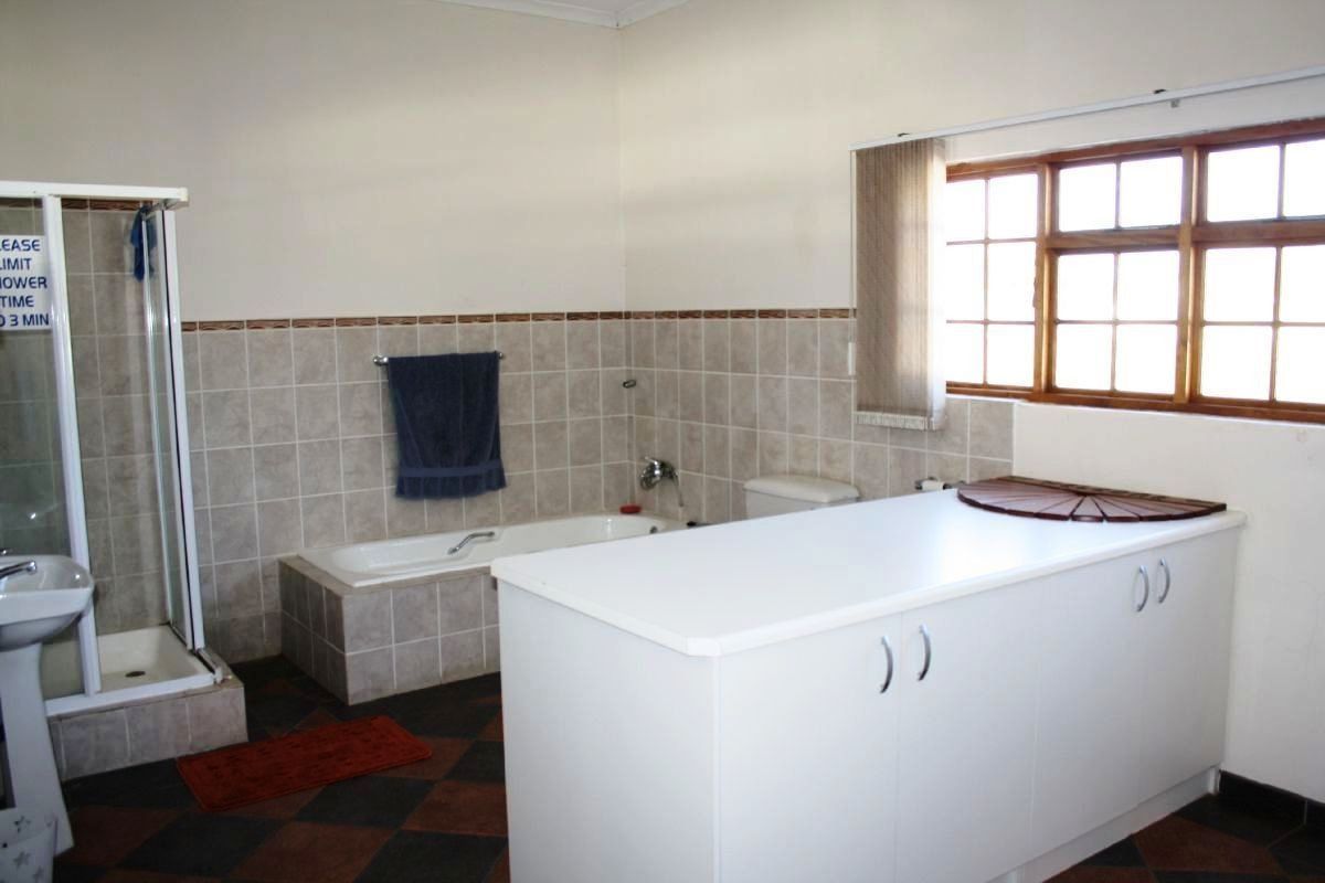 A functional bathroom featuring a built-in bathtub, separate shower enclosure, vanity unit, and tiled wall finishes with natural light from a large window.