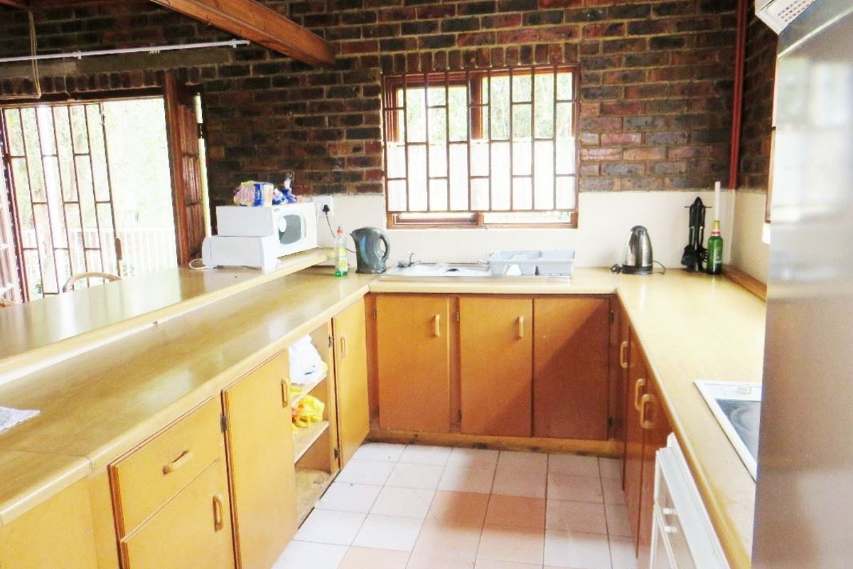 A functional kitchen featuring exposed brick walls, wooden cabinetry, laminate countertops, and ceramic tile flooring, offering a rustic aesthetic with potential for modernization.