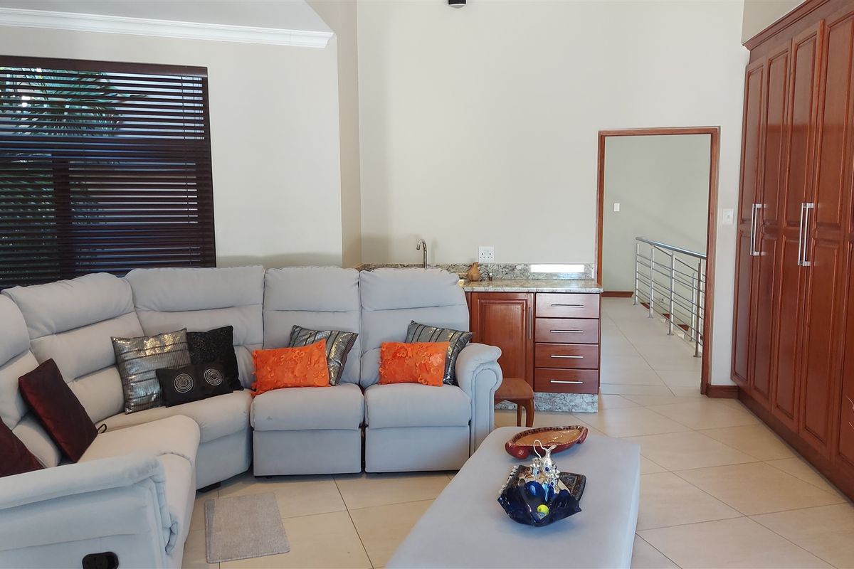 A spacious living area featuring built-in cabinetry, a wet bar with granite countertop, and large wooden blinds, leading to an adjacent hallway.
