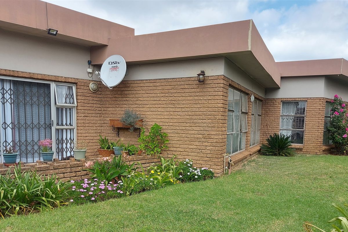 A view of the rear exterior of the house featuring brick masonry, security gates on windows, and a well-maintained garden area.