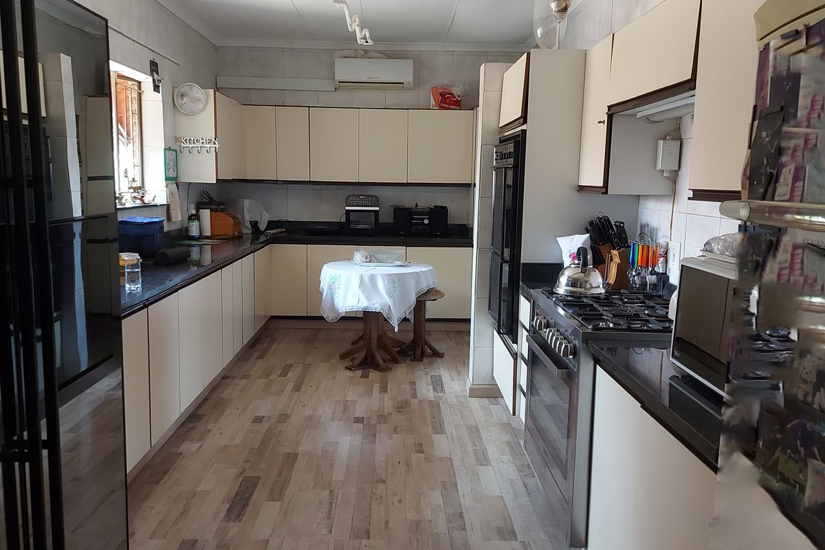 A functional kitchen featuring built-in cabinetry, a gas hob, an integrated oven, and a split-system air conditioner, finished with laminate flooring.