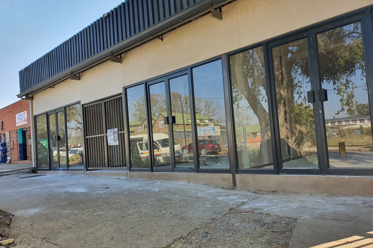 Front facade of a commercial property featuring extensive glass storefront windows, metal security gates, and a corrugated metal fascia detail.