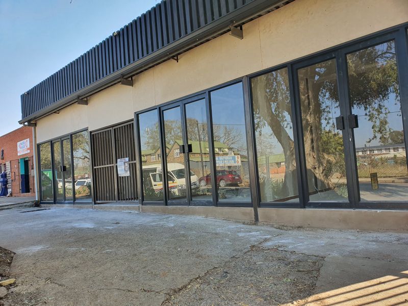 Front facade of a commercial property featuring extensive glass storefront windows, metal security gates, and a corrugated metal fascia detail.
