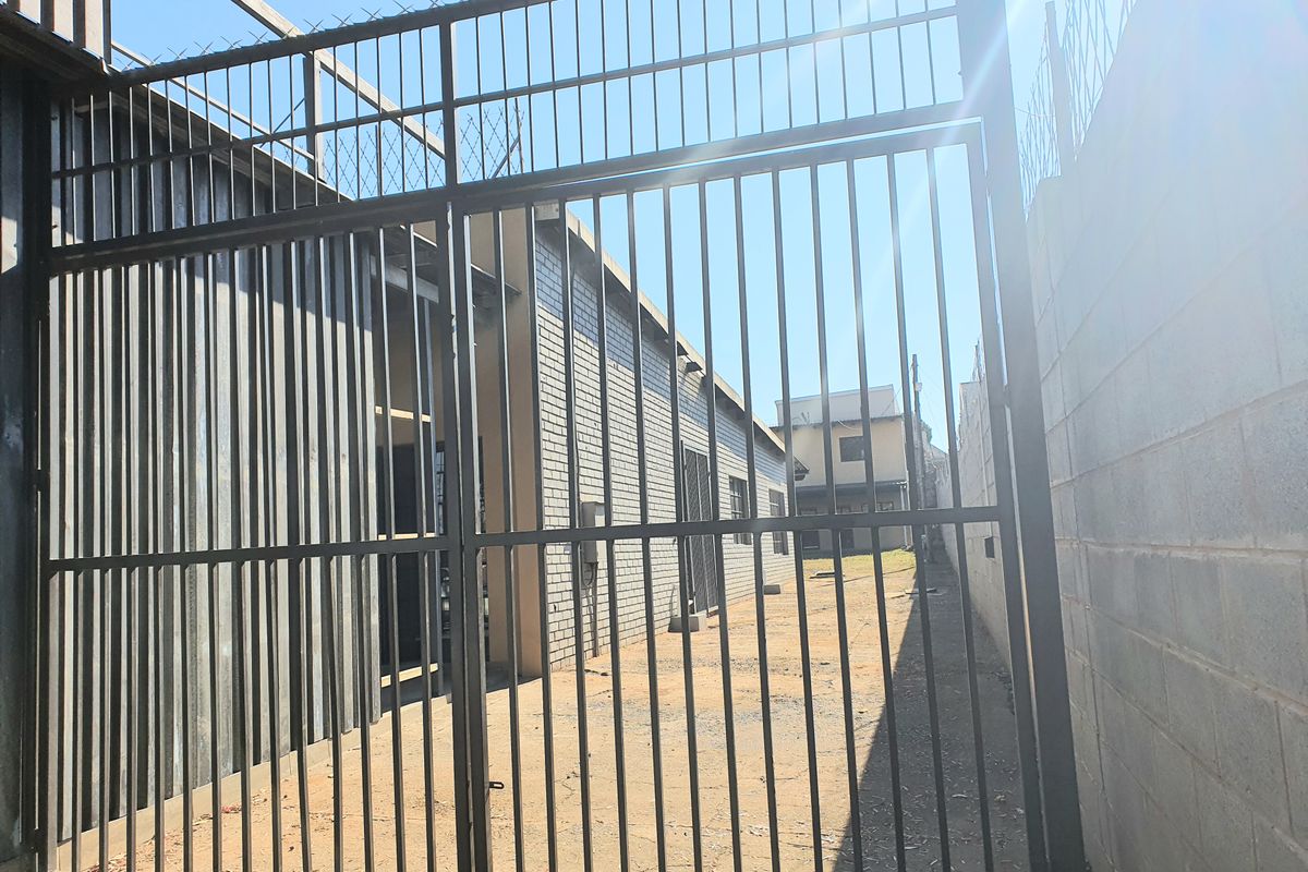 A secure rear exterior area featuring a metal gate, razor wire fencing, and brick boundary walls, providing access to the side of the building.
