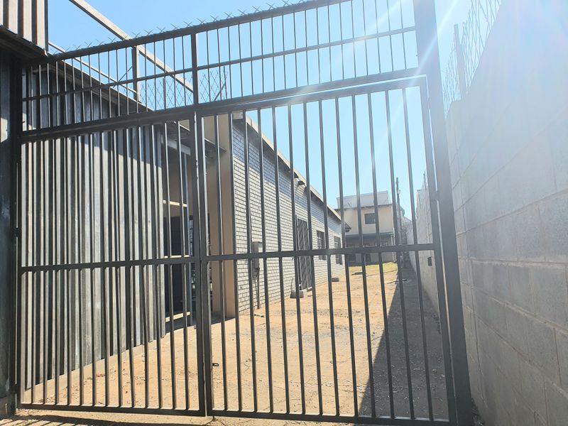 A secure rear exterior area featuring a metal gate, razor wire fencing, and brick boundary walls, providing access to the side of the building.