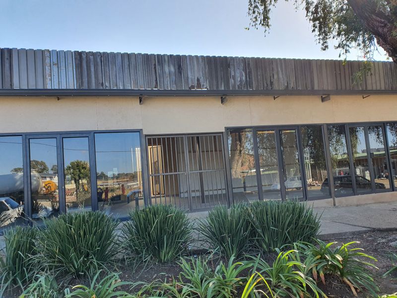 Front facade of a commercial building featuring large glass doors, security gates, and weathered metal roof cladding.