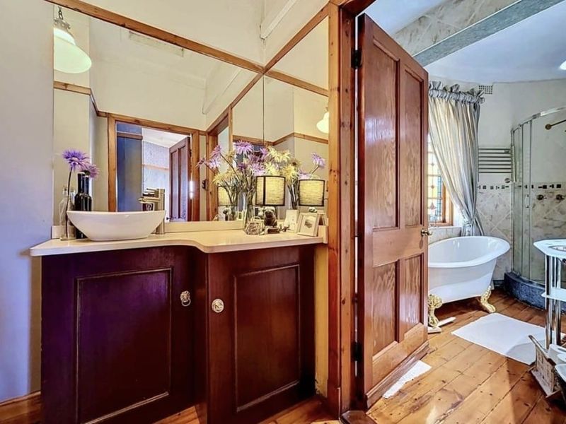 A well-maintained bathroom featuring a timber vanity with vessel sink, a classic clawfoot bathtub, and a separate corner shower enclosure with timber flooring.