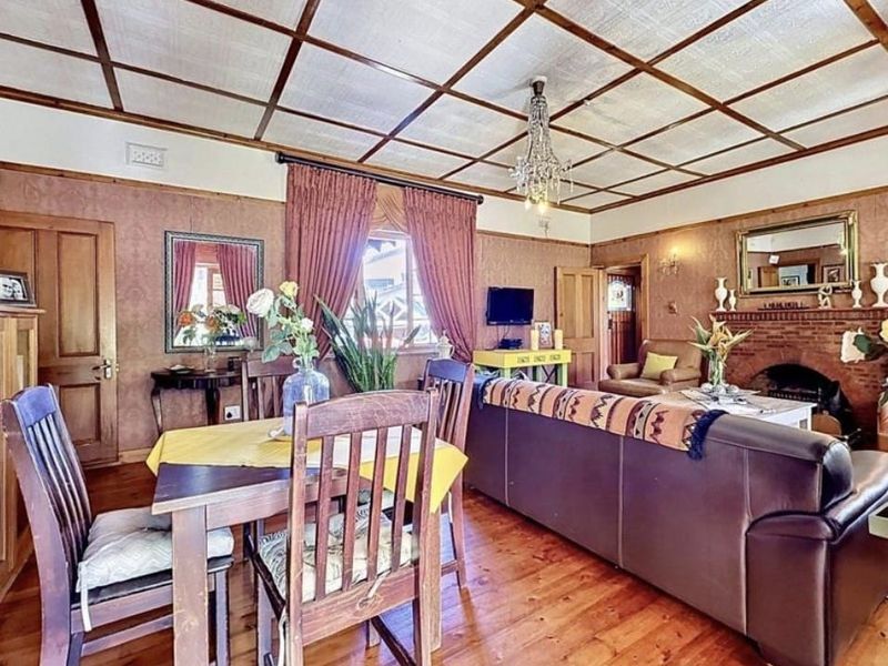 Open plan living and dining area featuring a brick fireplace, hardwood flooring, and a distinctive timber-grid ceiling.