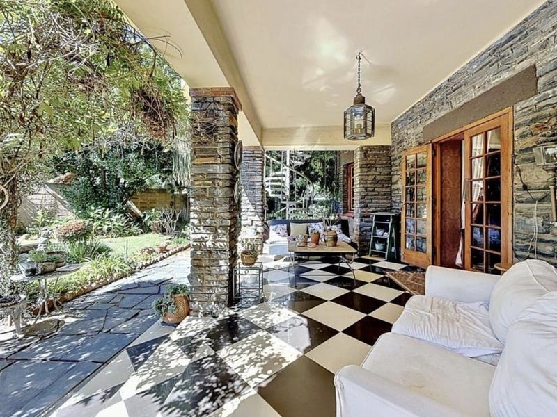 A covered patio featuring stone-clad pillars, checkerboard tile flooring, and a spiral staircase, providing direct access to the garden through timber-framed glass doors.