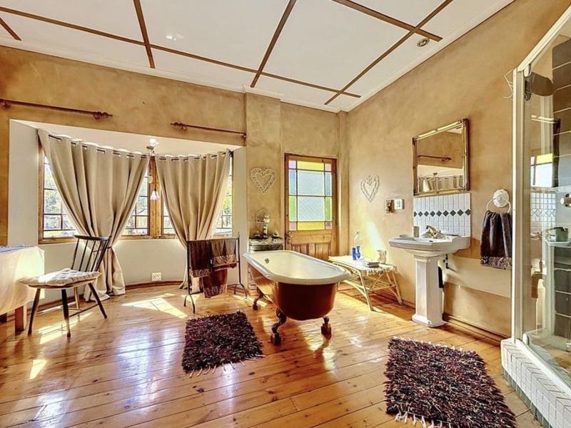 Spacious bathroom featuring a classic freestanding bathtub, pedestal sink, separate shower enclosure, and timber flooring with characterful stained glass door detailing.