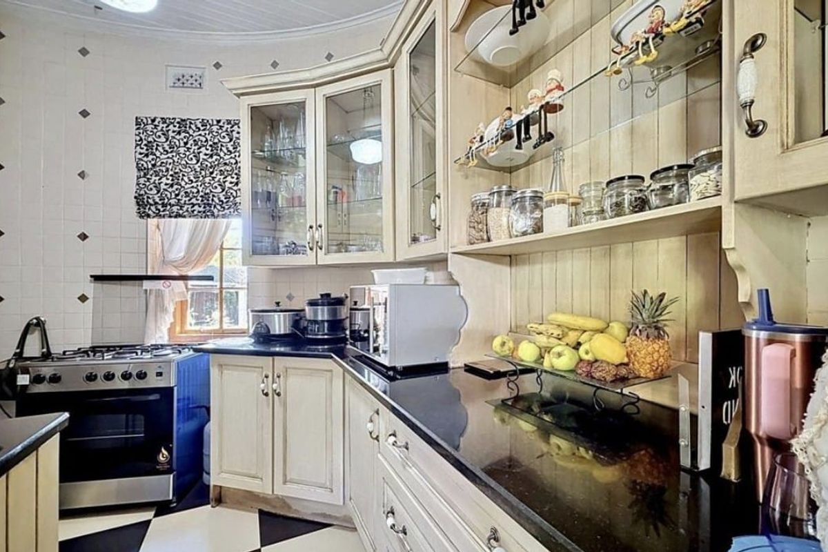 A classic kitchen featuring cream-toned cabinetry, black granite countertops, a gas stove, and decorative glass-fronted display units with a tiled backsplash.