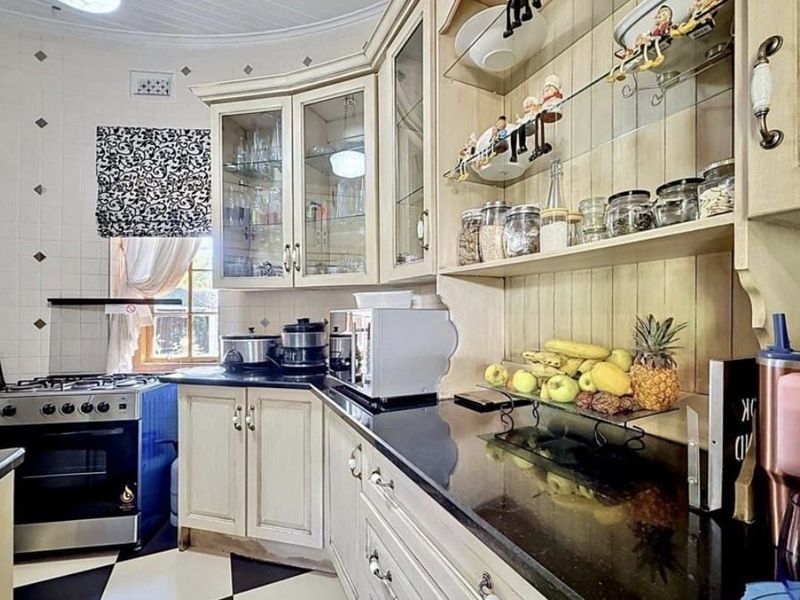 A classic kitchen featuring cream-toned cabinetry, black granite countertops, a gas stove, and decorative glass-fronted display units with a tiled backsplash.