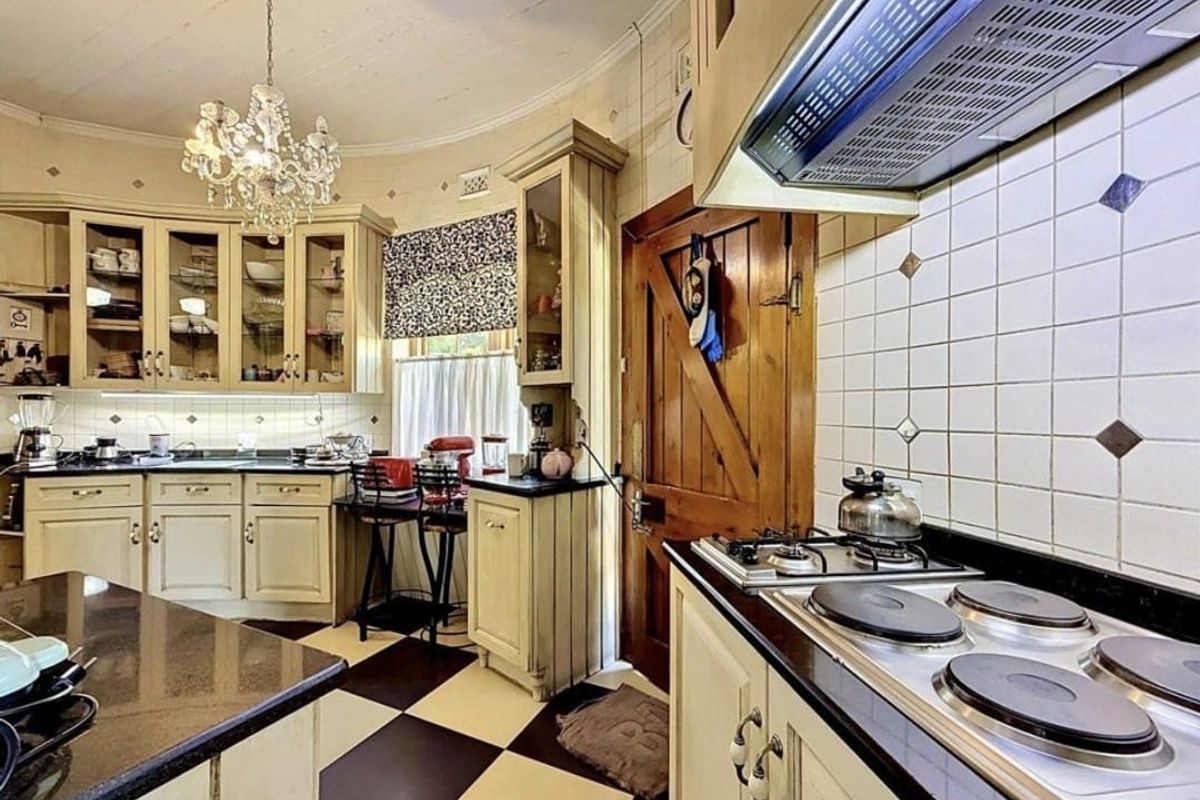 A classic kitchen featuring built-in cabinetry, granite countertops, a combination gas and electric hob with extractor fan, and distinctive checkerboard floor tiling.