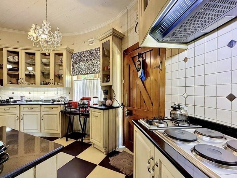 A classic kitchen featuring built-in cabinetry, granite countertops, a combination gas and electric hob with extractor fan, and distinctive checkerboard floor tiling.