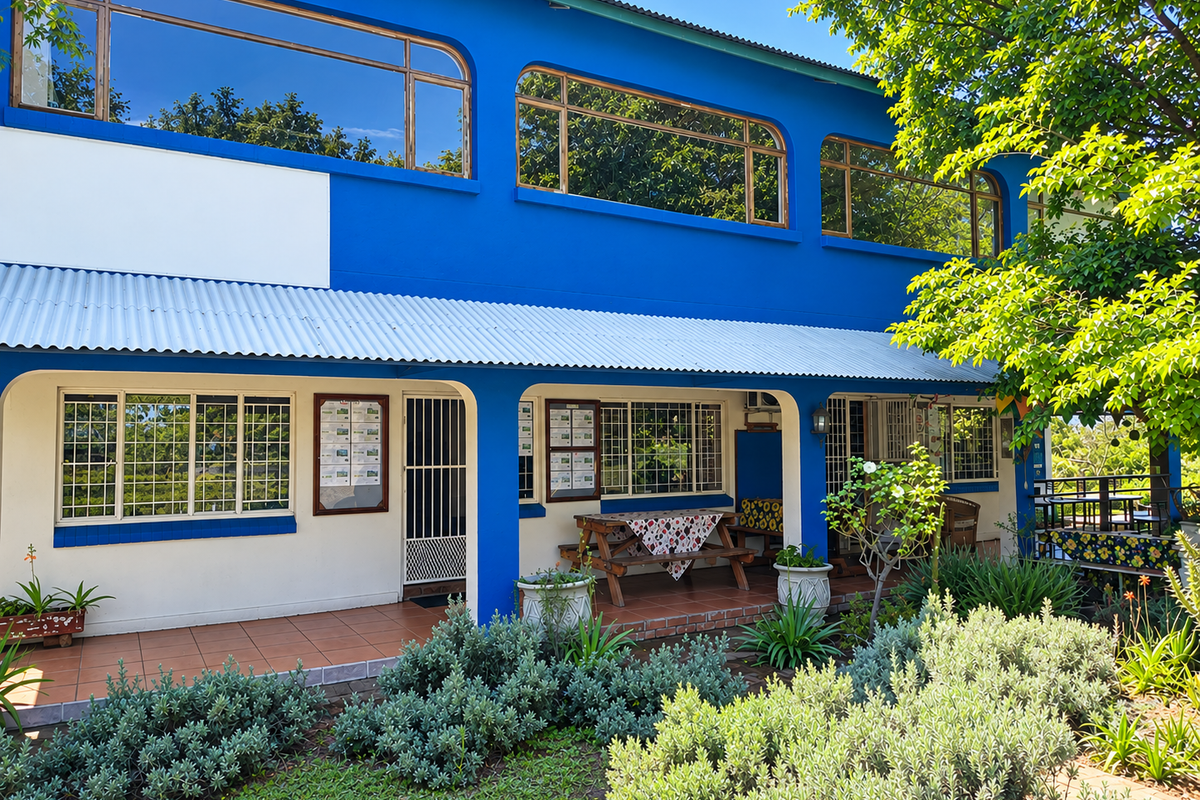 A two-story commercial building exterior featuring a blue facade, large windows, a covered tiled patio area, and a well-maintained garden.