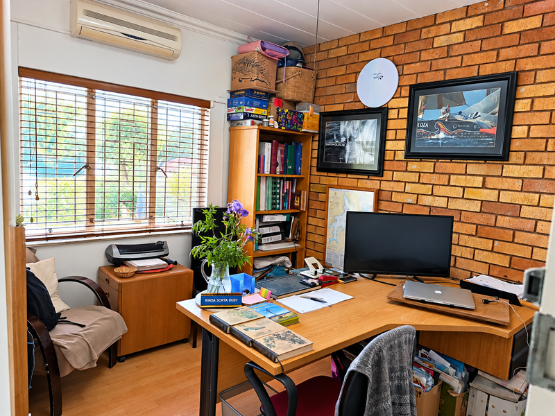 A functional home office featuring an exposed brick feature wall, laminate flooring, and a wall-mounted air conditioning unit with natural light from the window.