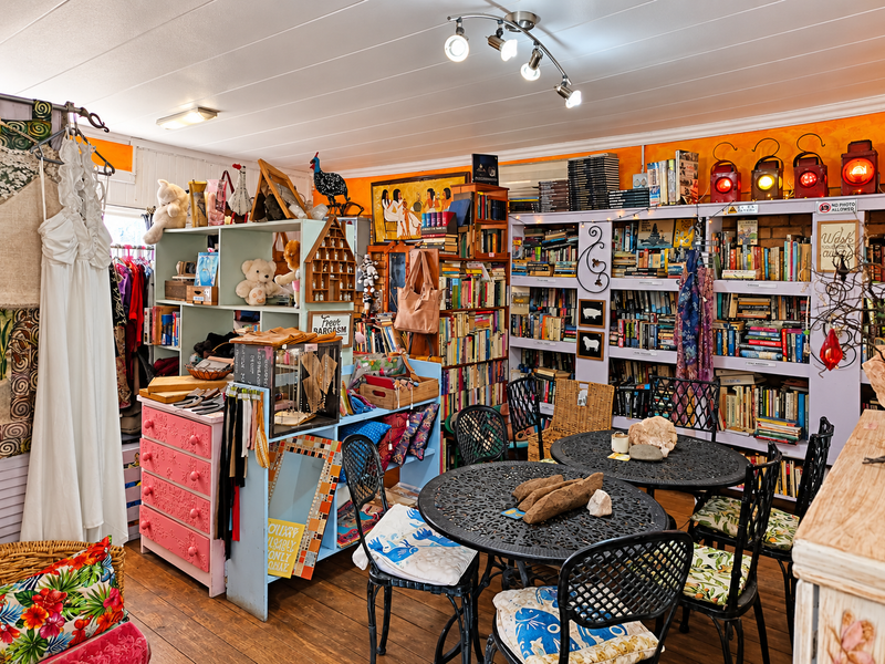A commercial retail space featuring extensive built-in shelving units, track lighting, and timber flooring, currently utilized for a variety of goods.