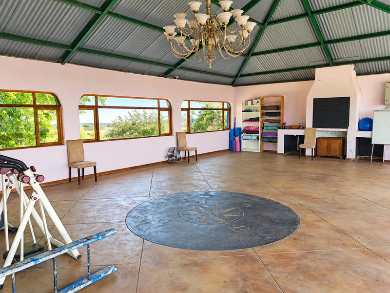 Spacious gym area featuring a high vaulted corrugated metal ceiling, large windows with scenic views, a built-in fireplace, and a decorative compass floor inlay.