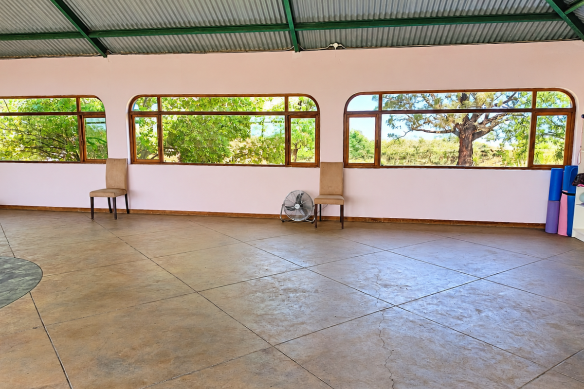 Spacious gym area featuring large windows with garden views, exposed steel roof trusses, and tiled flooring.