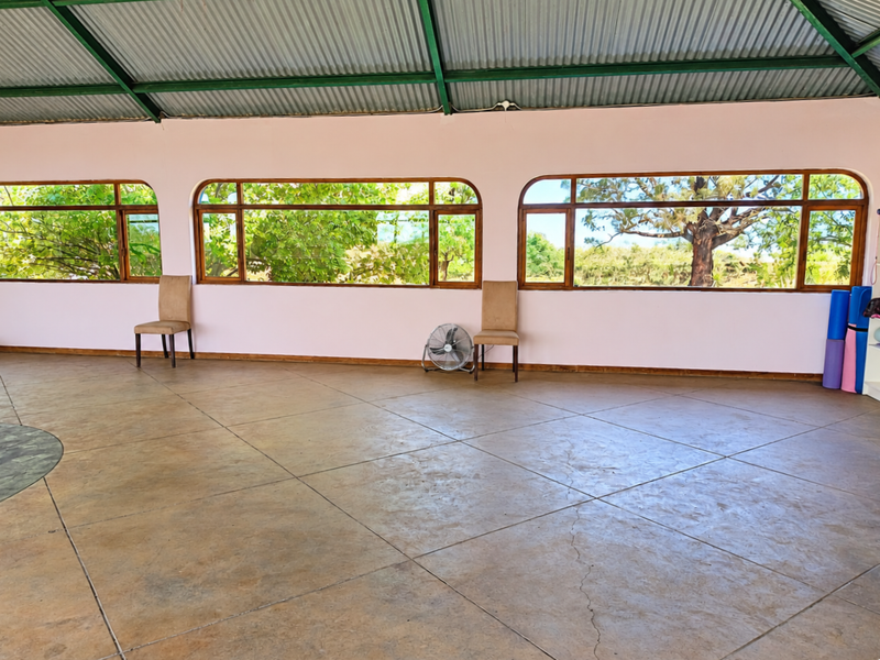 Spacious gym area featuring large windows with garden views, exposed steel roof trusses, and tiled flooring.