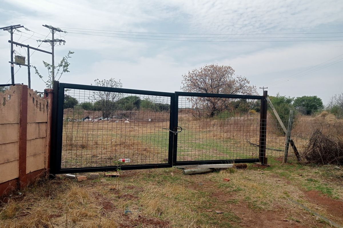A view of a metal mesh entrance gate and precast concrete boundary wall on a rural farm property.