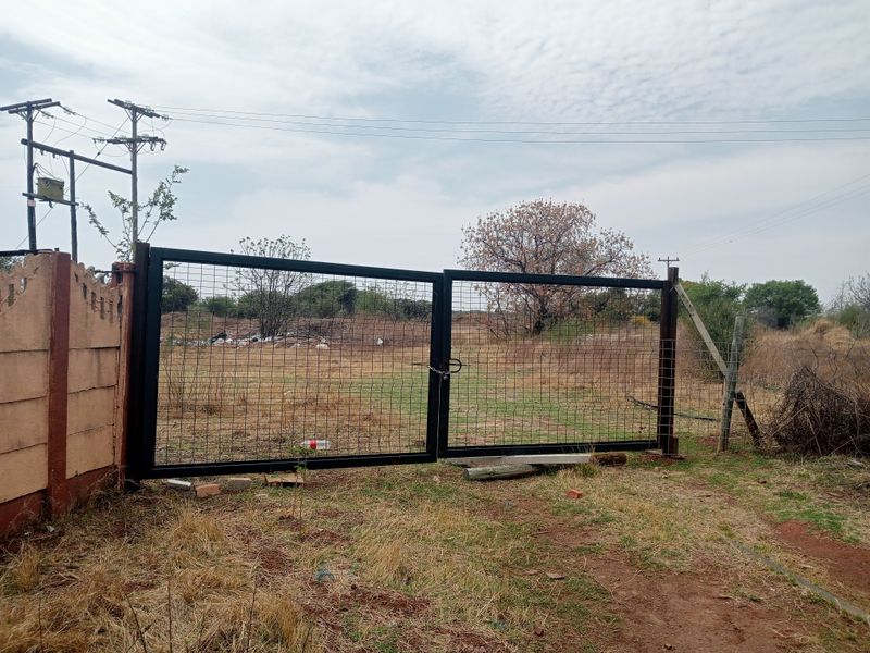 A view of a metal mesh entrance gate and precast concrete boundary wall on a rural farm property.