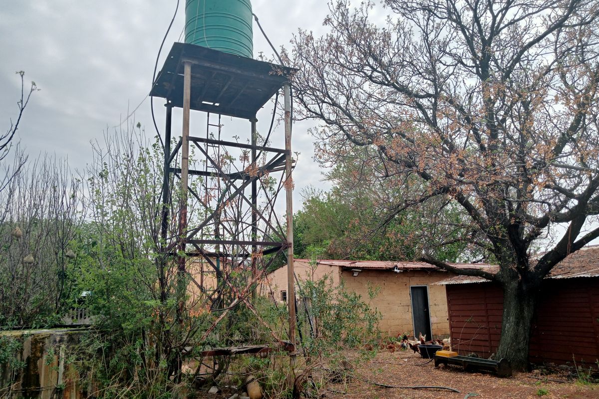 Rear farm yard area featuring an elevated water tank on a metal support structure, adjacent to a basic masonry outbuilding.