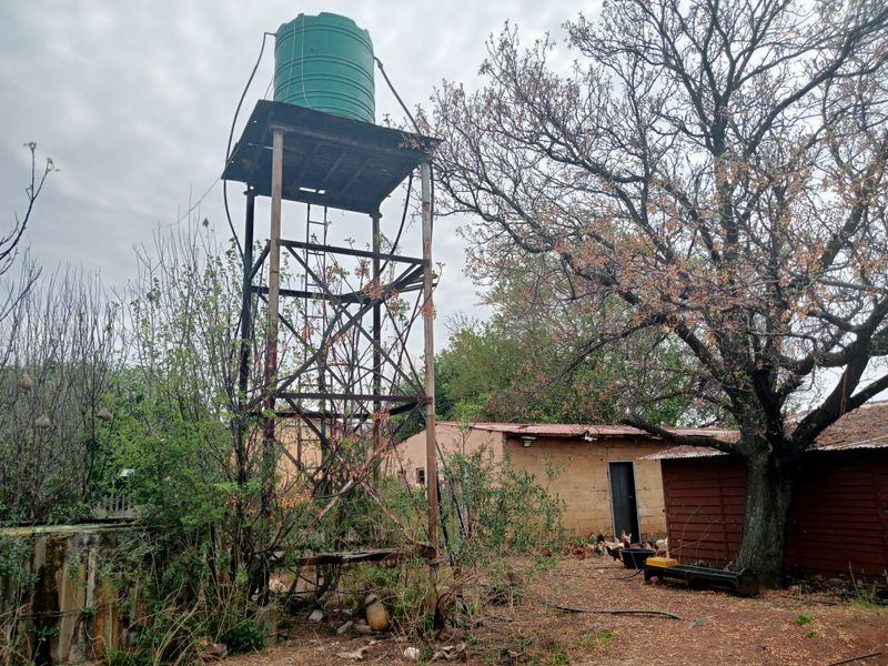 Rear farm yard area featuring an elevated water tank on a metal support structure, adjacent to a basic masonry outbuilding.