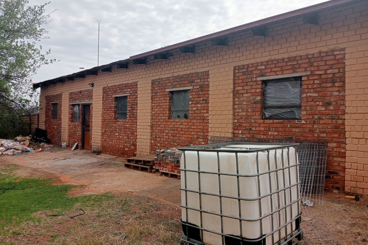 Rear view of a farm building featuring exposed brickwork, a corrugated metal roof, and concrete apron, currently requiring maintenance and exterior finishing.