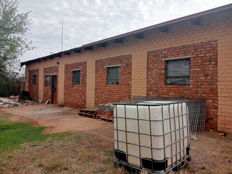 Rear view of a farm building featuring exposed brickwork, a corrugated metal roof, and concrete apron, currently requiring maintenance and exterior finishing.