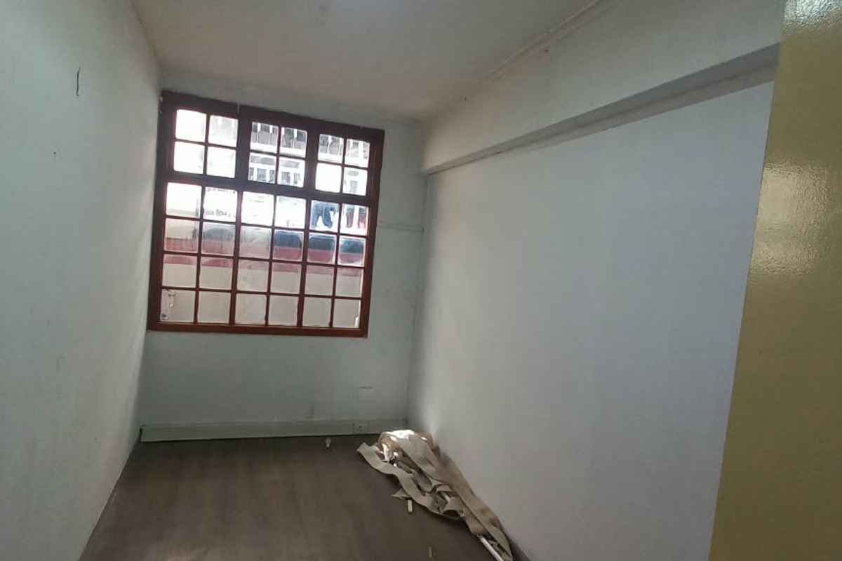 An empty office space featuring laminate flooring and a large grid-pattern window, offering a blank canvas for professional use.