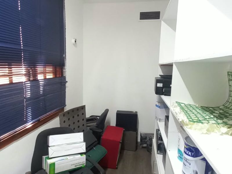A compact office space featuring built-in white shelving units, dark wood-look flooring, and blue venetian blinds.