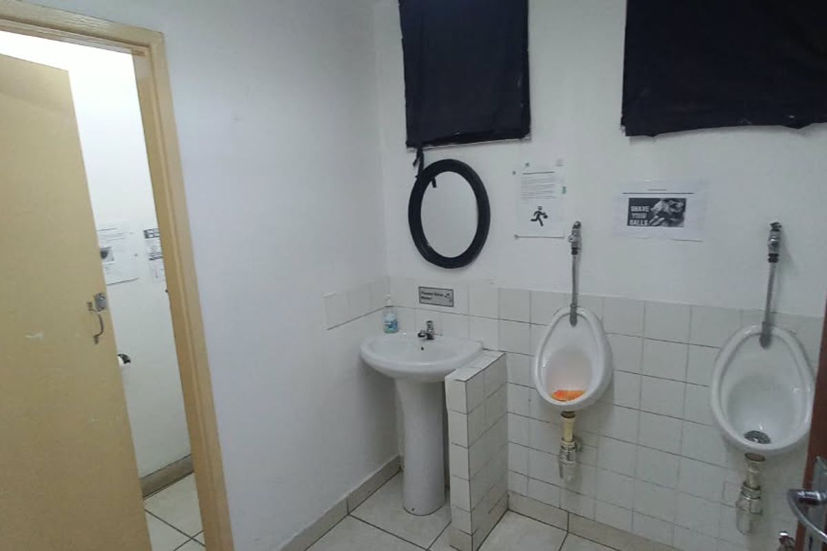 A functional office restroom featuring a pedestal washbasin and two wall-mounted urinals with tiled finishes.