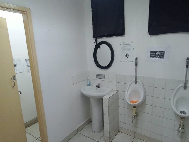 A functional office restroom featuring a pedestal washbasin and two wall-mounted urinals with tiled finishes.