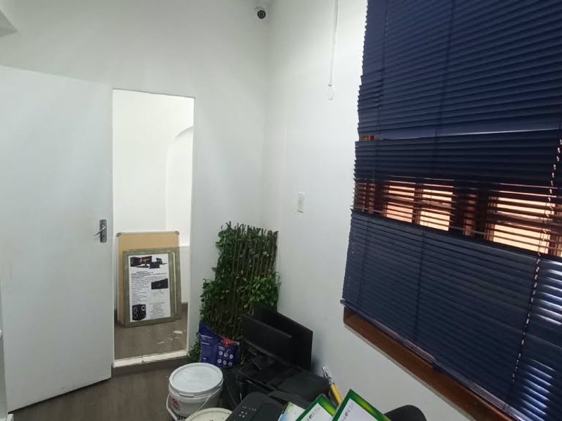 A functional office space featuring built-in shelving, dark laminate flooring, and blue venetian blinds, providing a practical workspace environment.