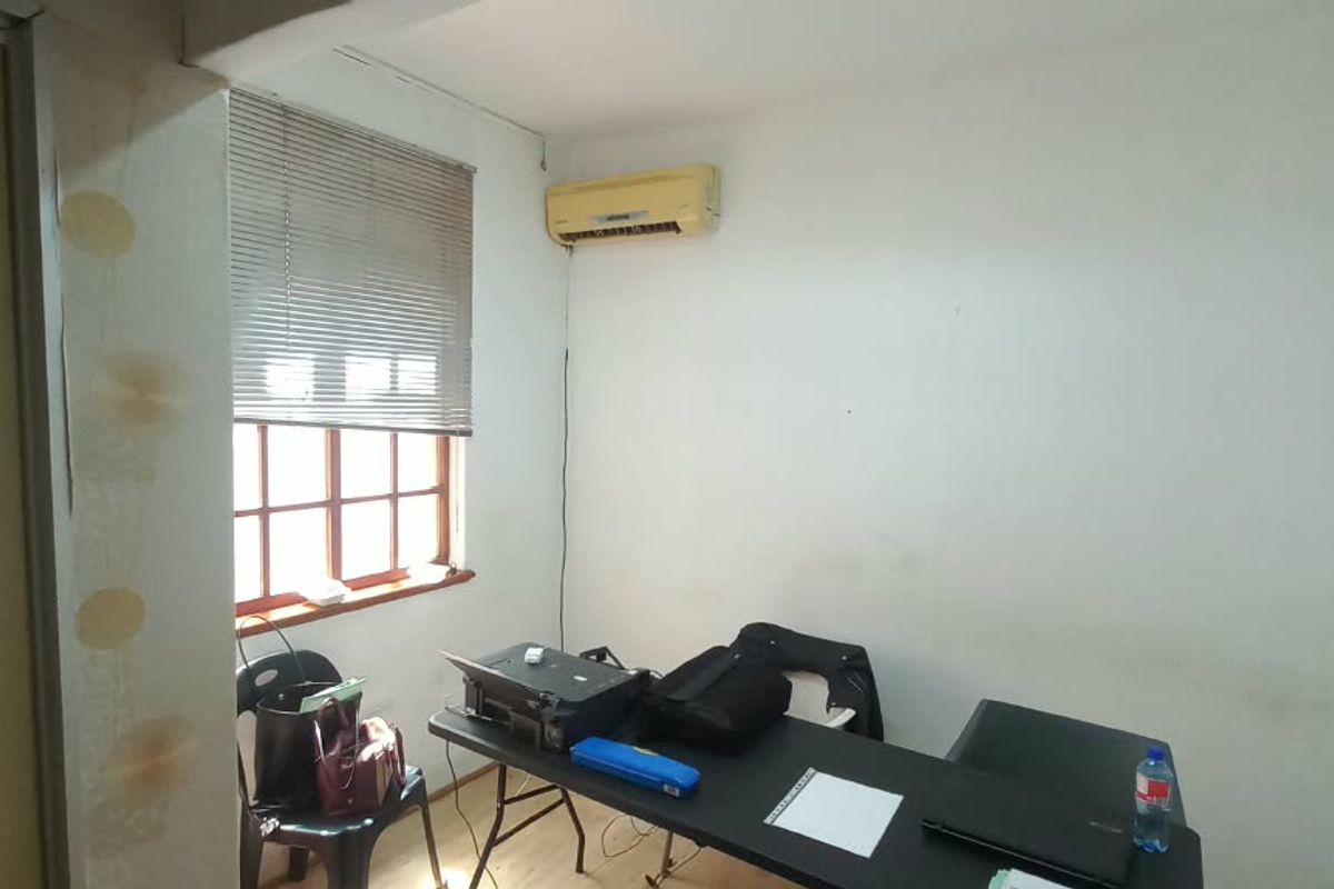 A functional office space featuring laminate flooring, an air conditioning unit, and a window with venetian blinds, requiring minor cosmetic updates.