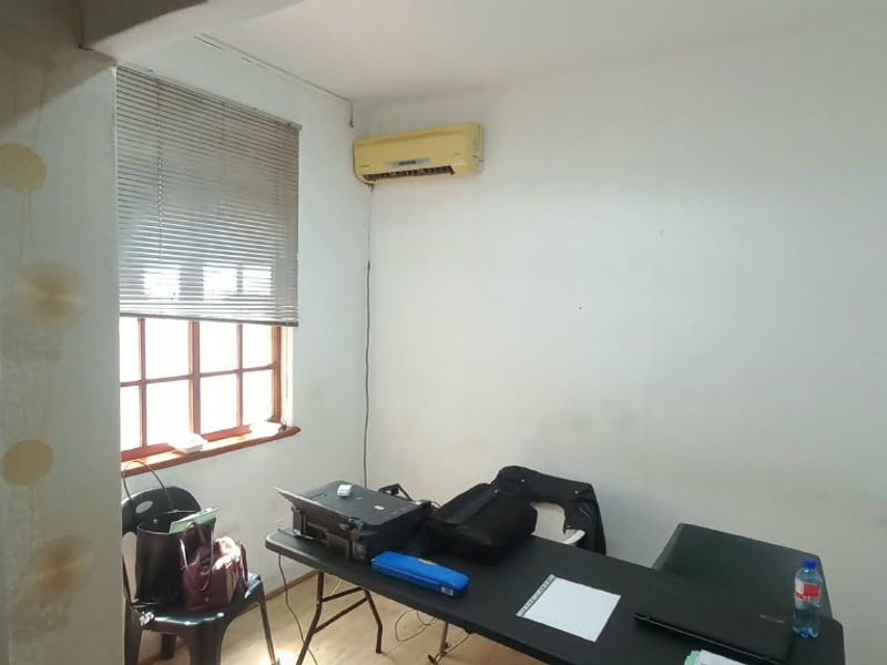 A functional office space featuring laminate flooring, an air conditioning unit, and a window with venetian blinds, requiring minor cosmetic updates.