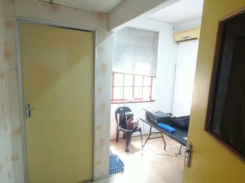 A small office space featuring laminate flooring, an air conditioning unit, and window blinds, currently used as a workspace.