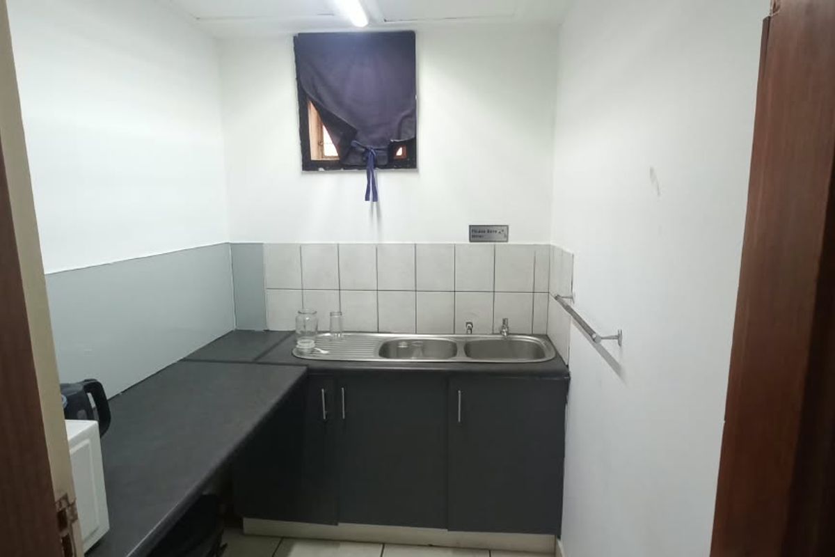 A compact kitchenette featuring a stainless steel sink, dark laminate countertops, and tiled backsplash, suitable for office staff use.