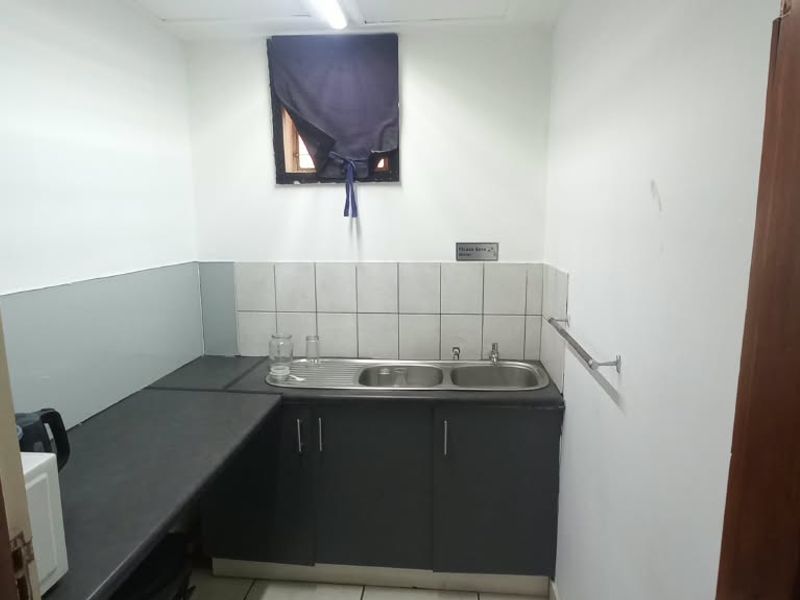 A compact kitchenette featuring a stainless steel sink, dark laminate countertops, and tiled backsplash, suitable for office staff use.