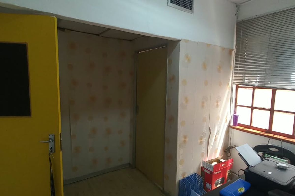 A functional office space featuring a multi-pane window with venetian blinds, air conditioning vent, and internal doors, currently requiring cosmetic wall updates.