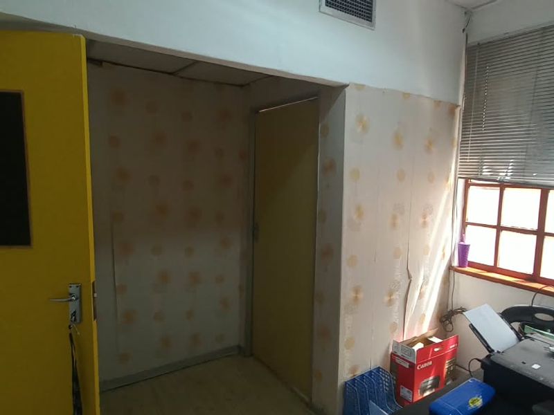 A functional office space featuring a multi-pane window with venetian blinds, air conditioning vent, and internal doors, currently requiring cosmetic wall updates.