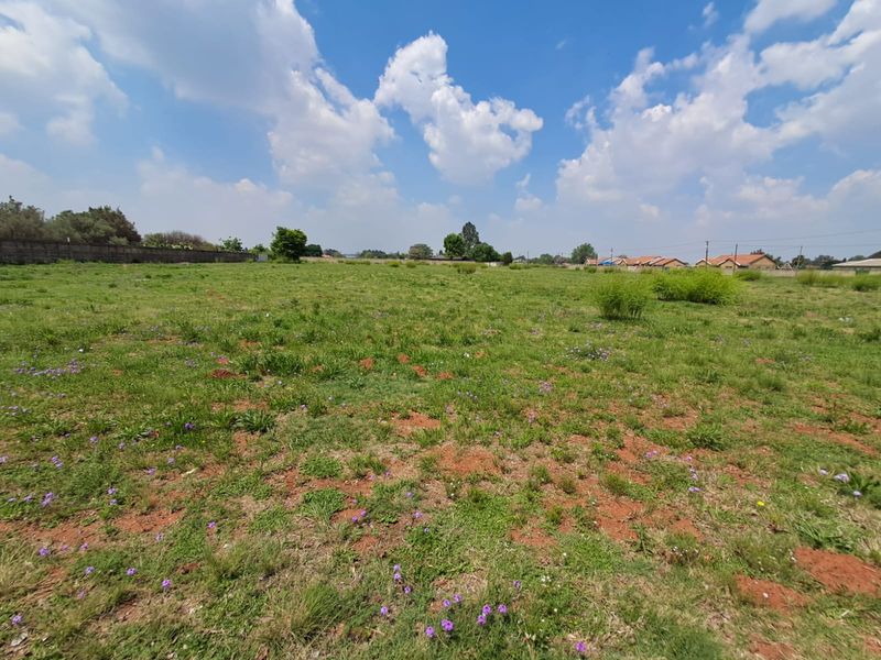 A wide-angle view of a vacant commercial land plot featuring natural grass coverage and a perimeter boundary wall in the background.