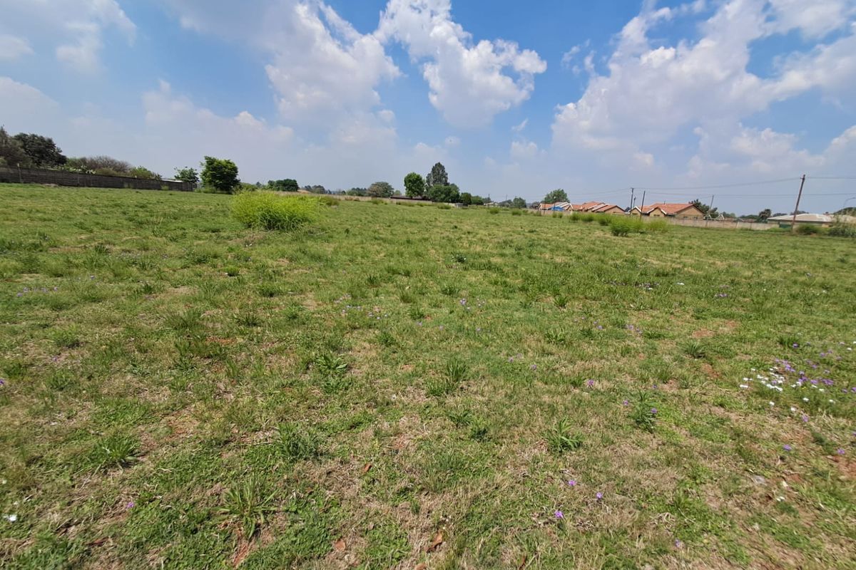 A wide-angle view of a vacant commercial plot featuring open grass terrain and surrounding perimeter walls.