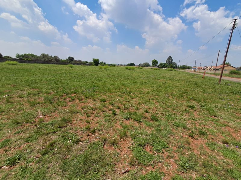 A wide-angle view of a vacant commercial land plot featuring grass coverage, perimeter boundary walls, and adjacent utility infrastructure.