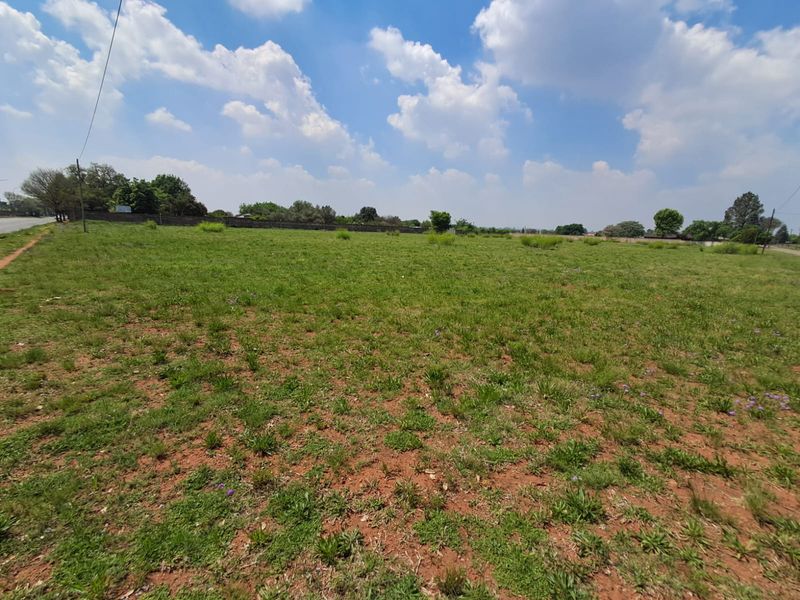 A wide-angle view of a vacant commercial land plot featuring open grass terrain and a perimeter boundary wall.