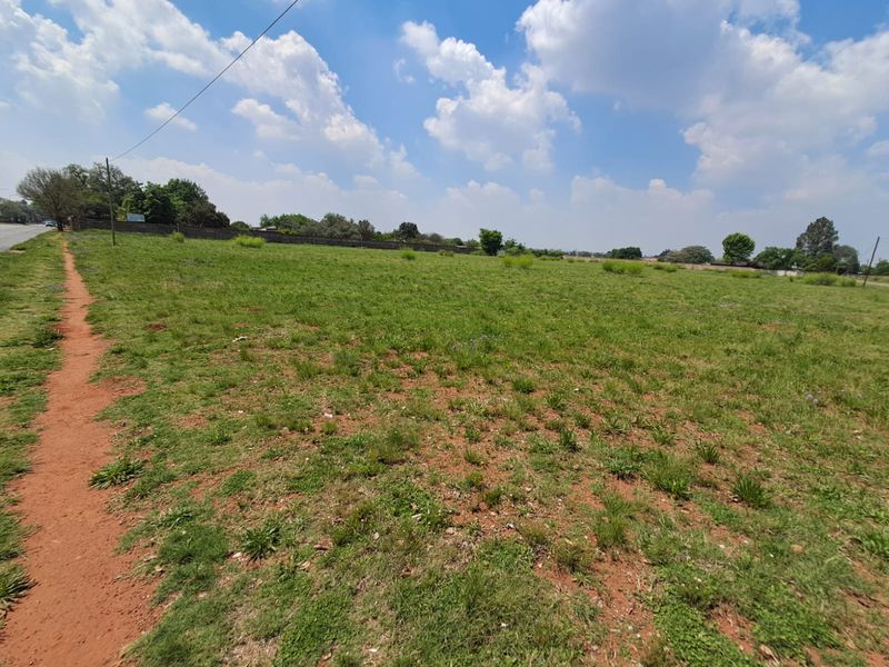 A wide-angle view of a vacant commercial land plot featuring open grass terrain and a perimeter boundary wall.